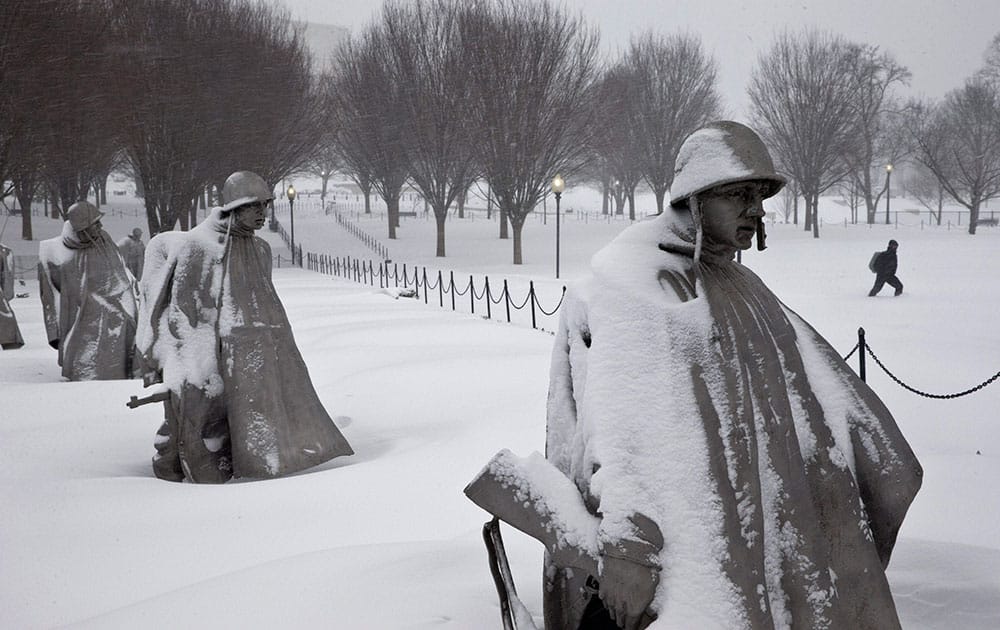 A pedestrian walks near the Korean War Veterans Memorial in the snow.