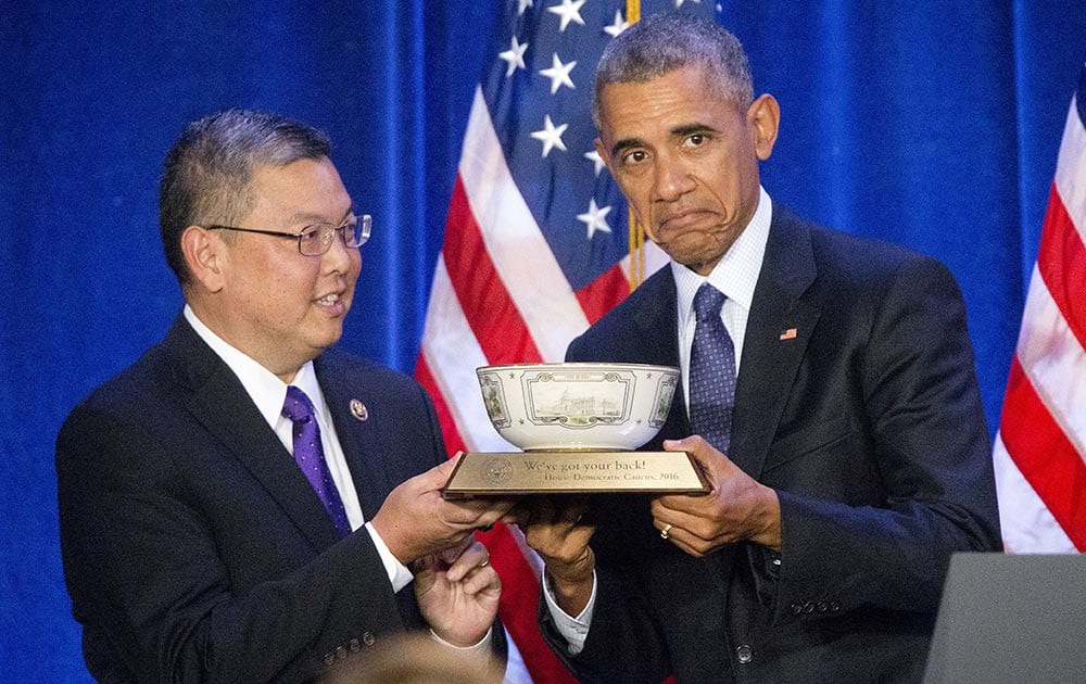 President Barack Obama, is presented a commemorative bowl by Rep. Mark Takai, D- Hawaii, left, before speaking at the House Democratic Issues Conference in Baltimore, Md.