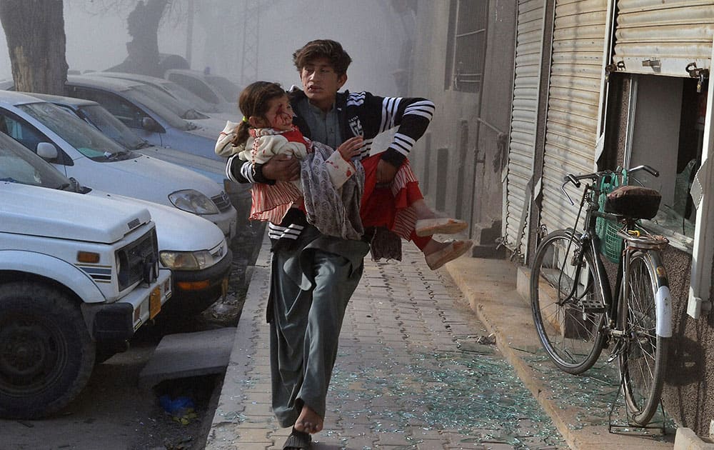 An injured boy carries an injured girl as he runs towards a safe area a few minutes after the suicide bombing in Quetta, Pakistan.