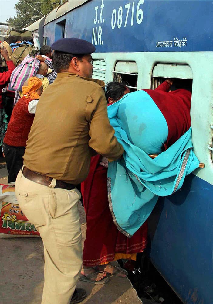 A Railway Protection Force(RPF) Constable pushing a woman through a window to board a train as pilgrims return homes after taking holy dip in river Ganges on the occasion of Mauni Amavasya in Allahabad.