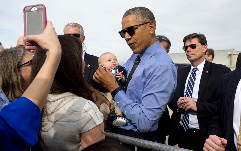 President Barack Obama hold a small child while greeting guests on the tarmac by before boarding Air Force One at Moffett Federal Airfield in Mountain View, Calif.