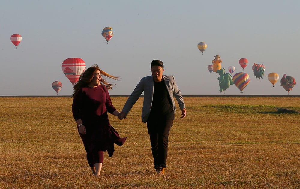 A couple holds hands with hot air balloons in the background at Clark Air Field, Pampanga province north of Manila, Philippines on the eve of Valentine's Day.