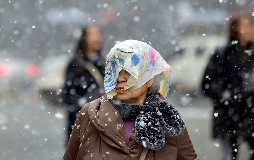 A woman covers her head with a scarf against heavy snow in Seoul, South Korea.