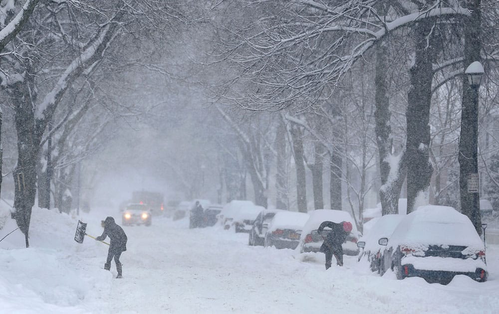 People shovel snow from around cars and parking spots along a street in Rochester, N.Y., during a snowstorm.