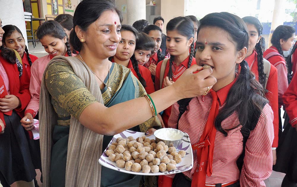 Teacher offers sweets to students at an examination centre before they appear for CBSE examinations in Moradabad.