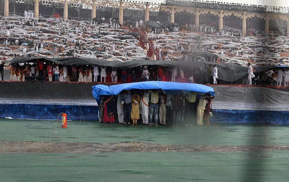 Delegates trying to protect themselves under plastic sheets as it rains during the opening day of the three-day long World Culture Festival on the banks of Yamuna River in New Delhi