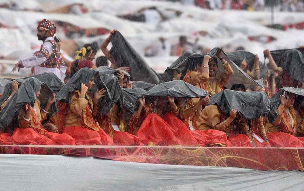 Performers trying to protect themselves with plastic sheets as it rains during the opening day of the three-day long World Culture Festival on the banks of Yamuna River in New Delhi.