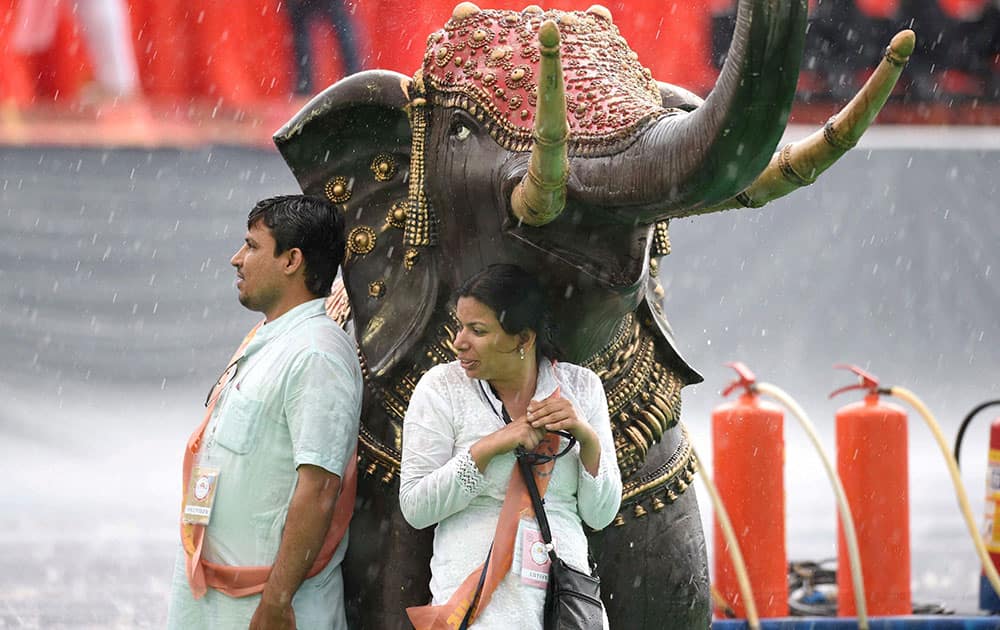 Performers trying to protect themselves under an elephant statue as it rains during the opening day of the three-day long World Culture Festival on the banks of Yamuna River in New Delhi.