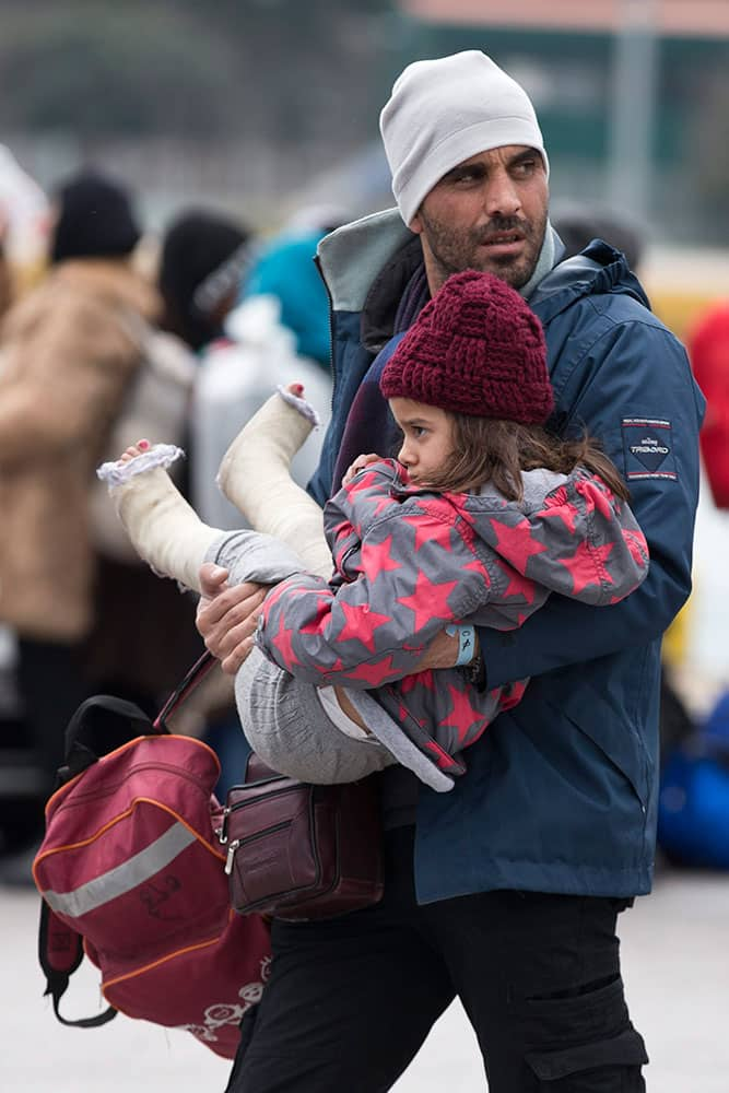 A Syrian man carries a child as migrants and refugees who just arrived with a ferry from Greek island prepare to get on busses with destination a transit camp at the port of Piraeus near Athen.