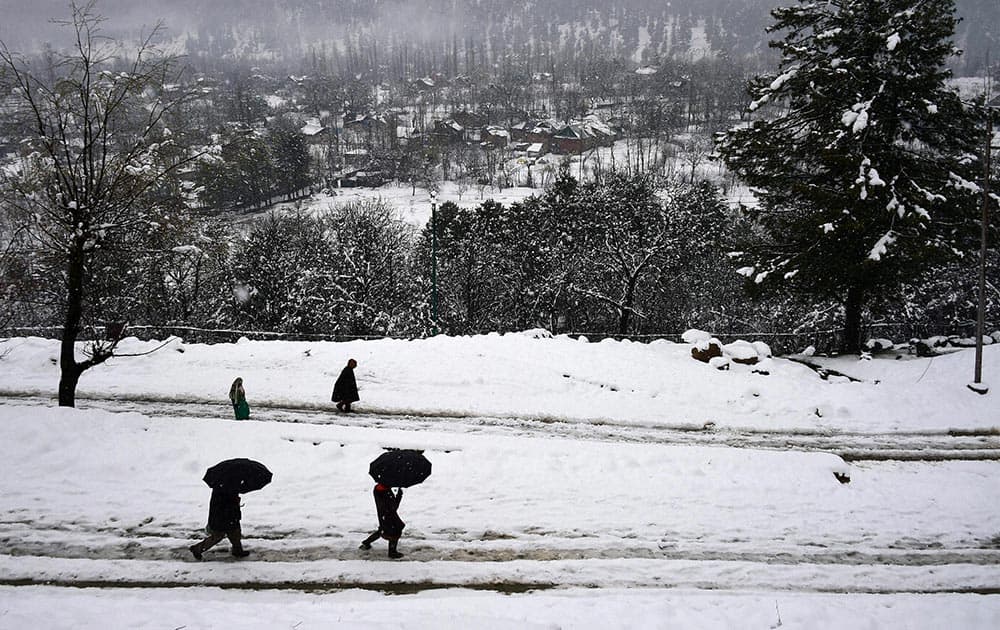 People walk with umbrellas during fresh snowfall at Tangmarg in Baramulla District of North Kashmir.