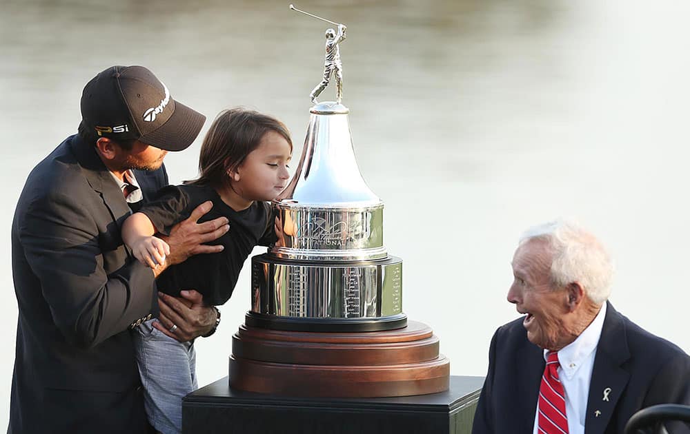 Arnold Palmer, right, smiles as he watches Jason Day, of Australia, hoist his son Dash up to kiss the championship trophy after Day won the Arnold Palmer Invitational golf tournament in Orlando, Fla.