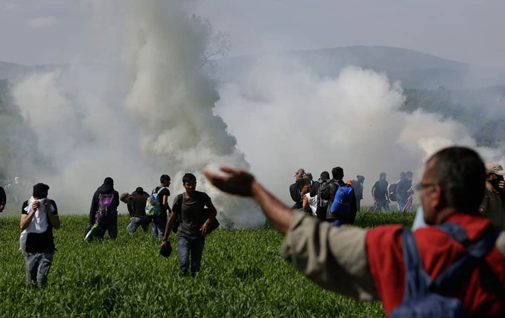 A group of migrant men run away from tear gas used by Macedonian police after migrants broke a fence at the northern Greek border point of Idomeni, Greece.