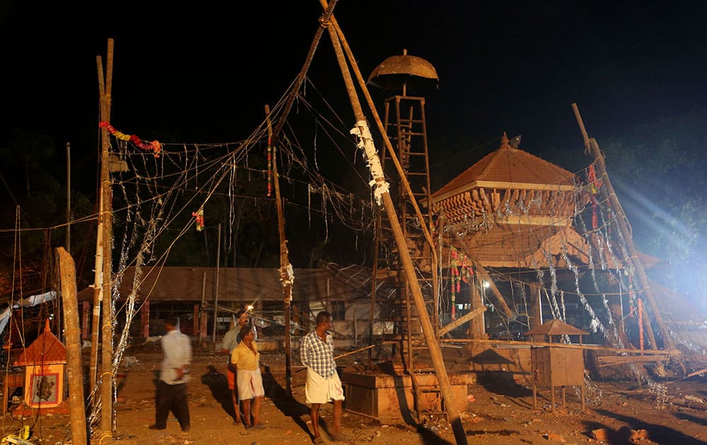 People walk past the damaged structures at the spot where a massive fire broke out during a fireworks display at the Puttingal temple complex in Paravoor village, Kollam district, southern Kerala state.