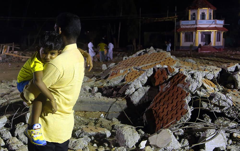 A man carries his child as he walks past the debris of a damaged building at the spot where a massive fire broke out during a fireworks display at the Puttingal temple complex in Paravoor village, Kollam district, southern Kerala state.