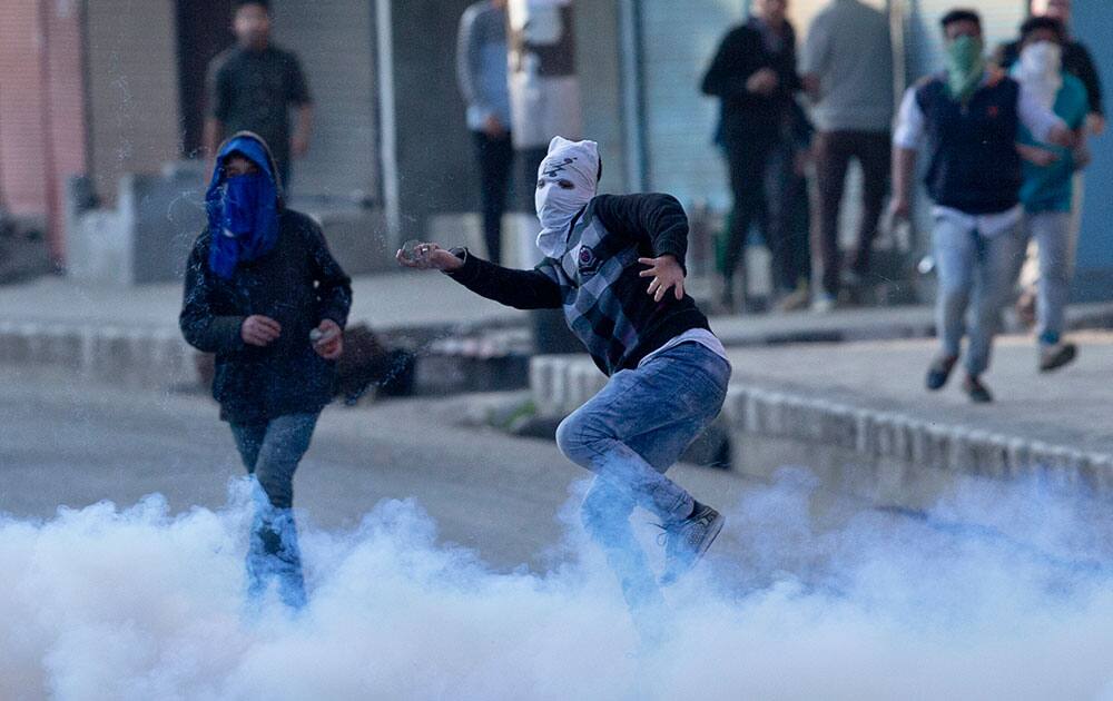 A protester throws rocks and bricks at Indian policemen amid tear gas smoke during a protest in Srinagar, India.