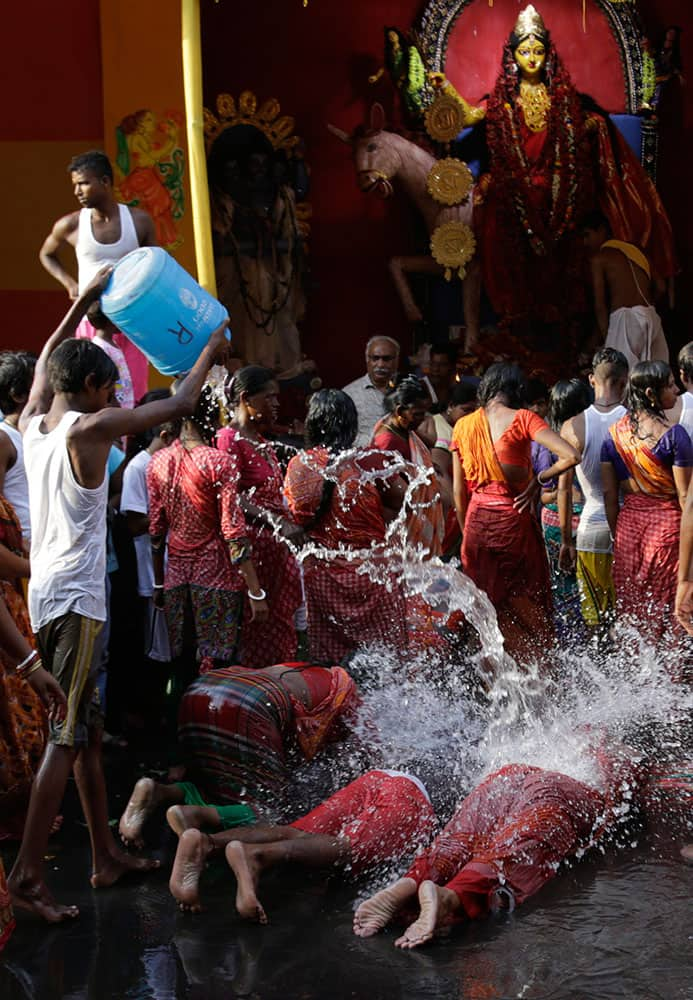 A boy pours water over Hindu devotees prostrating as part of rituals on Sitala Puja, dedicated to the Hindu goddess of pox, in Kolkata.