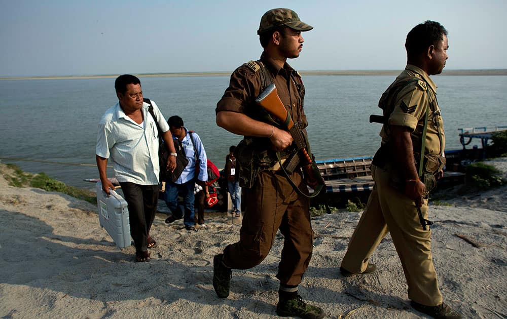Polling officials and security personnel with electronic voting machines walk after crossing the river Brahmaputra by boat at Bhatkhowa Chapori west of Guwahati, Assam.
