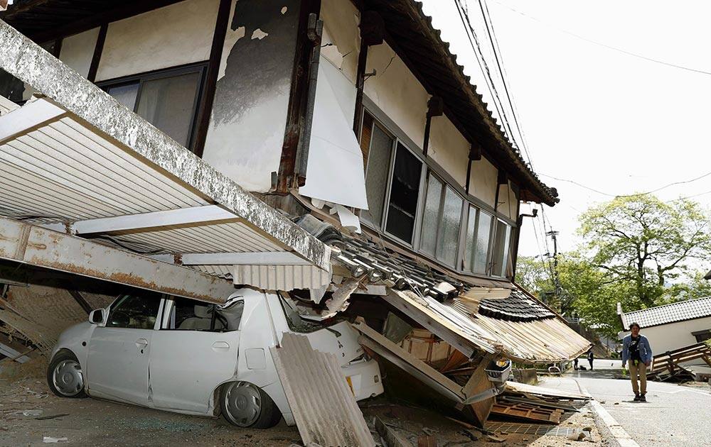 A car sits crushed by a house damaged in Thursday's earthquake in Mashiki, Kumamoto prefecture, southern Japan.