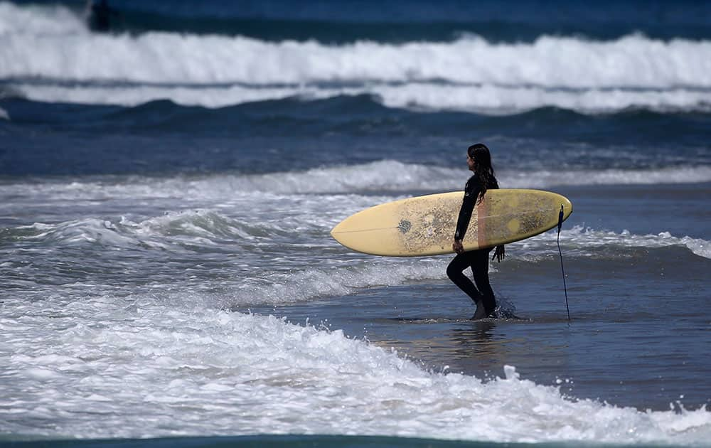 A surfer strolls into the waves a Cardiff State Beach where warm temperatures prevail in Encinitas, Calif. 