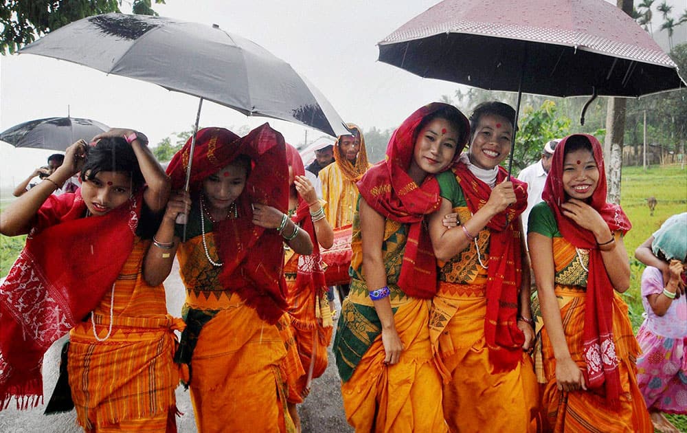 Bodo girls try to save themselves from rains with umbrellas while taking part in Gohain Ulliwa Festival at Mayong in Morigaon.