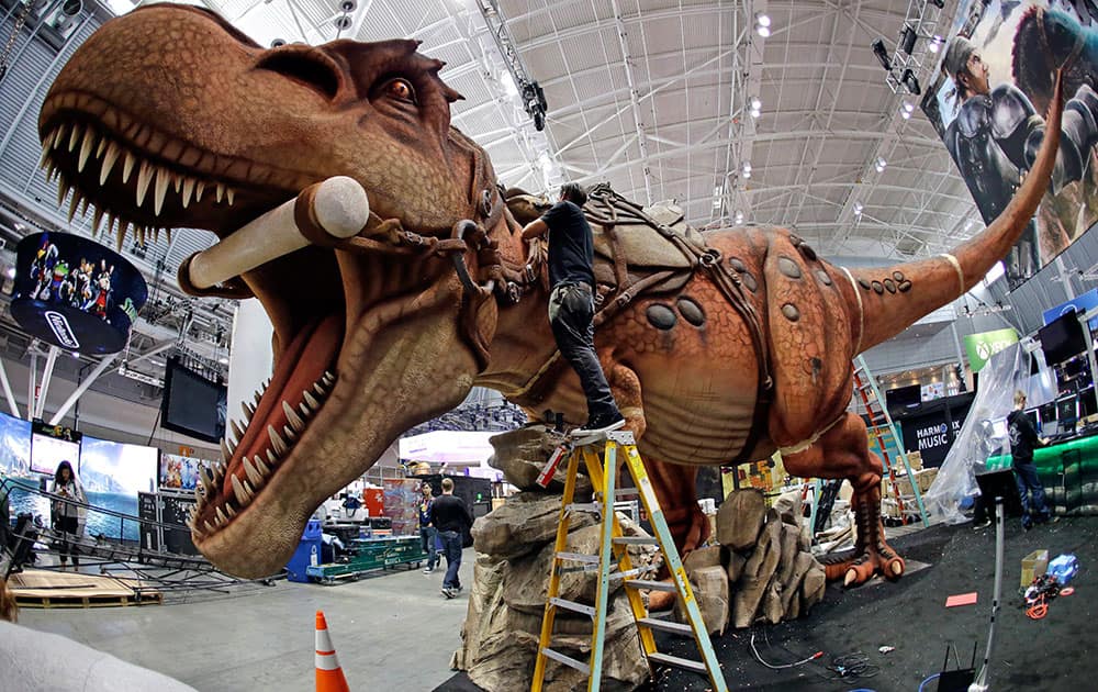 Joshua Patino stands on a ladder to put finishing touches on a giant dinosaur exhibit at PAX East in the Boston Convention and Expo Center, in Boston.