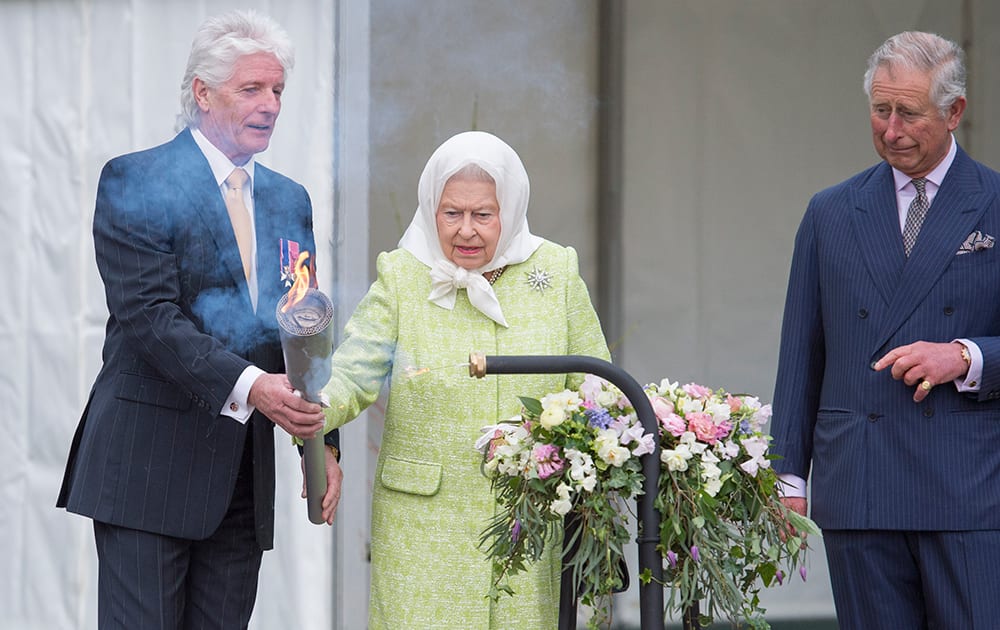 Britain's Queen Elizabeth II is handed a torch by Bruno Peek, Originator & Pageantmaster, with which to light the principal beacon to celebrate her 90th birthday, watched by her eldest son, Prince Charles.