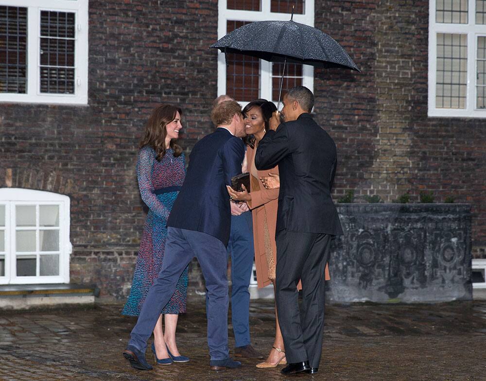 His Royal Highness Prince Harry of Wales leans into kiss first lady Michelle Obama as she and President Barack Obama are also greeted by the Duke and Duchess of Cambridge as they arrive at Kensington Palace in London.