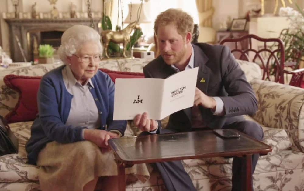 This image taken from a video released by Kensington Palace, London, on Friday April 29, shows Queen Elizabeth II sitting with her grandson, Prince Harry looking at an Invictus Games brochure. Prince Harry, released the video Friday promoting the upcoming Invictus Games for wounded veterans.