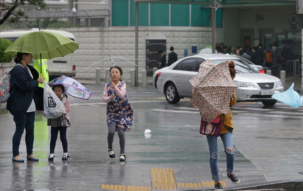 Passers-by try to manage their umbrellas in rain and strong wind in downtown Seoul, South Korea.