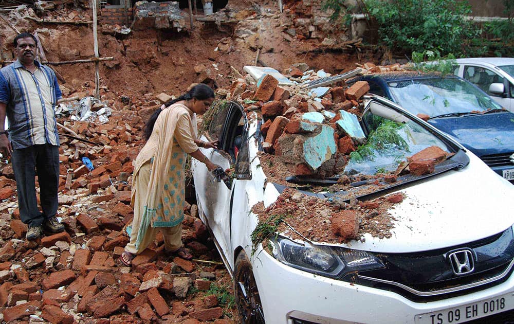 A woman checks her car damaged due to collapse of a wall during a storm, in Hyderabad.