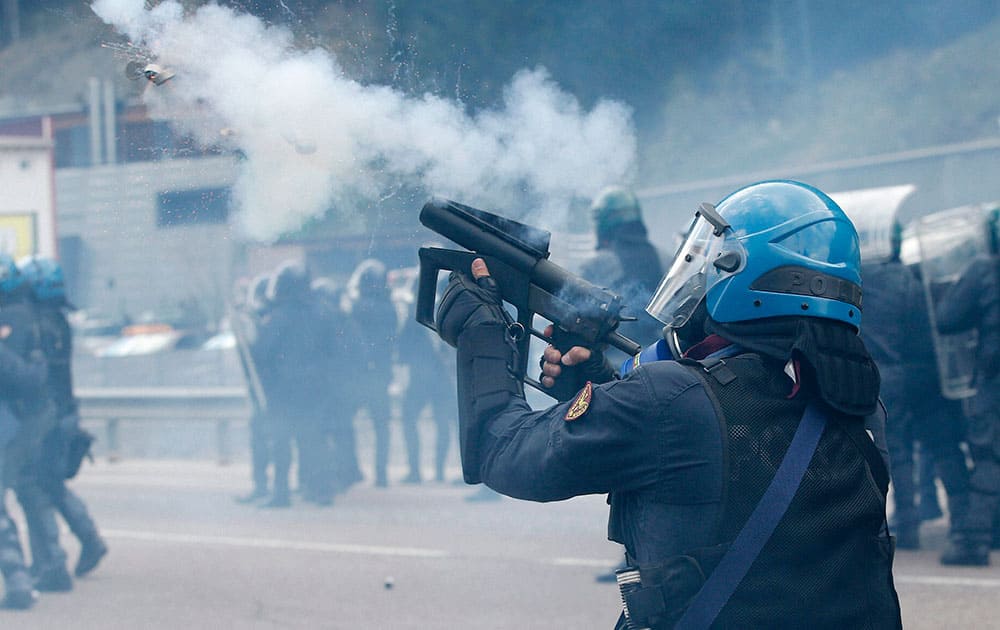 A riot police officer launches tear gas during a protest by anarchists against plans to tighten border controls to prevent the passage of migrants, in Brennero, Italy.