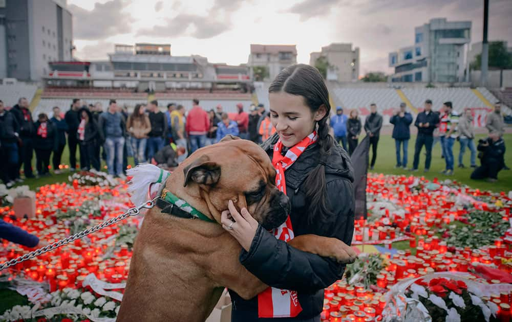 A Dinamo Bucharest fan hugs Sami the bullmastiff dog, back dropped by candels lit on the pitch in memory of midfielder Patrick Ekeng, who died after collapsing during a league match on Friday night in Bucharest, Romania.