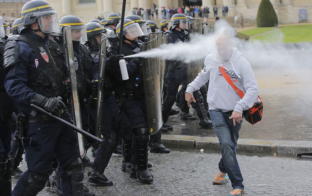 French riot police officers sprays pepper gas at a demonstrator during a protest against Labor Law as the Socialist government decided to force the bill through Parliament without a vote, in Paris.