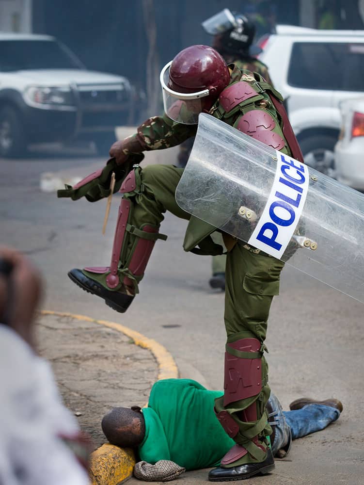 A Kenyan riot policeman repeatedly kicks a protester as he lies in the street after tripping over while trying to flee from them, during a protest in downtown Nairobi, Kenya.