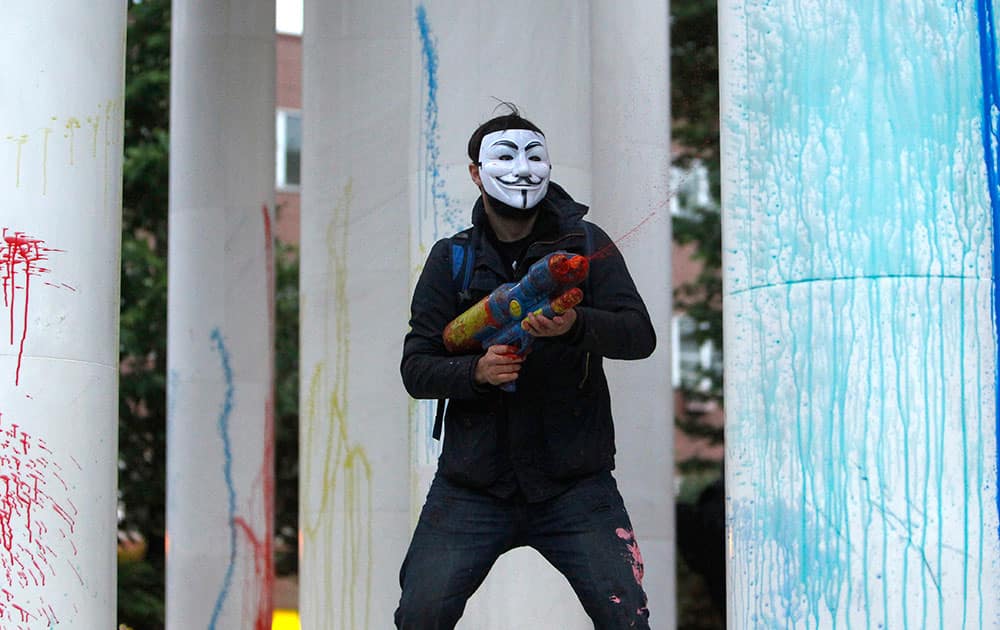 A protestor wearing a mask uses a water gun to spray colored paint on marble columns of a monument, during an anti-government protest in Skopje, Macedonia.