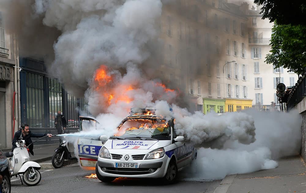 A man tries to pull off fire on a burning police car during clashes while police forces gather to denounce the almost daily violent clashes at protests against a labor reform in Paris. 