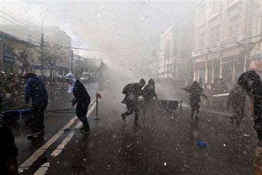 Protesters run from an approaching anti-riot vehicle blasting water, near Congress where President Michelle Bachelet was presenting the state-of-the-nation report, in Valparaiso, Chile.