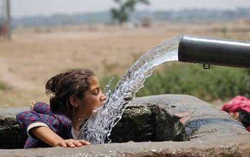 A girl drinks water from an irrigation tube, on a hot summer afternoon on the outskirts of Jammu, India.