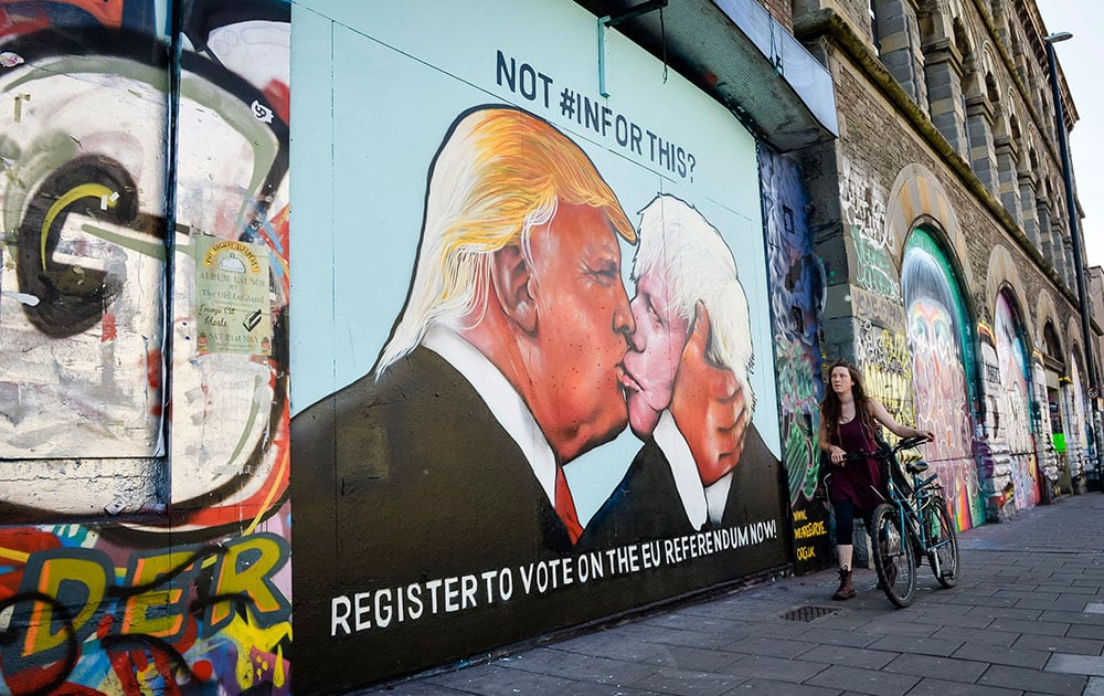 A woman walks past a political graffiti mural calling for people to register for the upcoming UK referendum depicting US presidential candidate Donald Trump and former London mayor Boris Johnson kissing, which is sprayed on a disused building in Bristol, England.