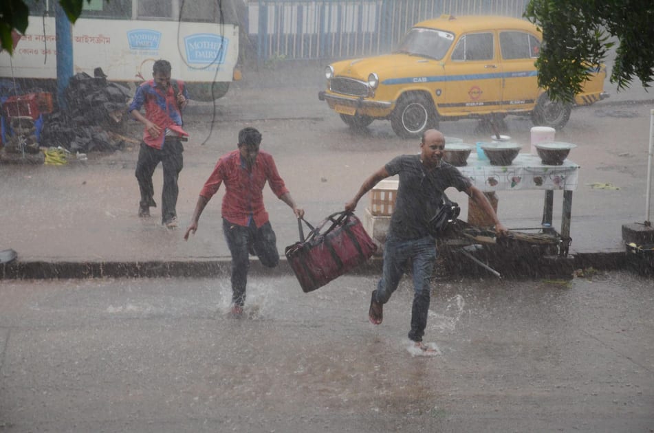 People, holding their bags, run to find a shed as it rains in Kolkata.