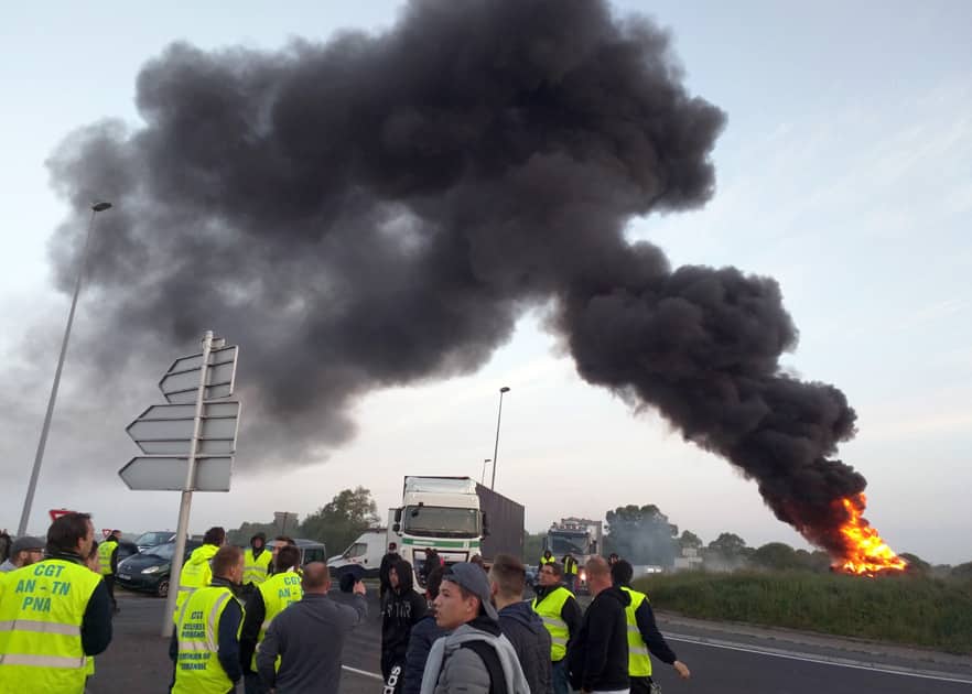 Union activists guard a traffic circle near the Normandie Bridge outside of Le Havre where a pile of burning tires gas thrown up a big cloud of smoke during a blockade action.