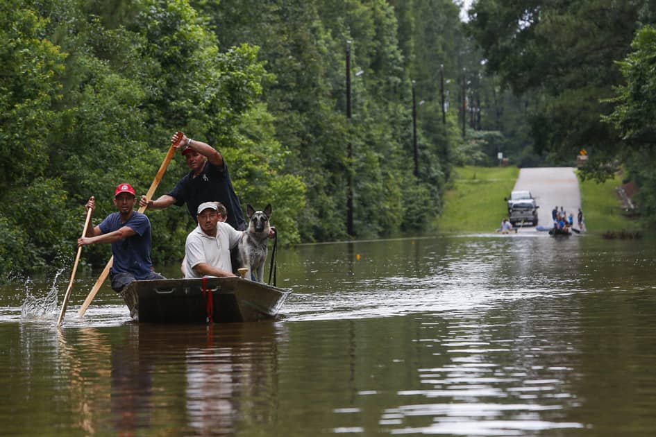 Roland Courville steers a boat across Mill Creek Road as he helps people escape from a neighborhood cut off by a flooded Spring Creek.