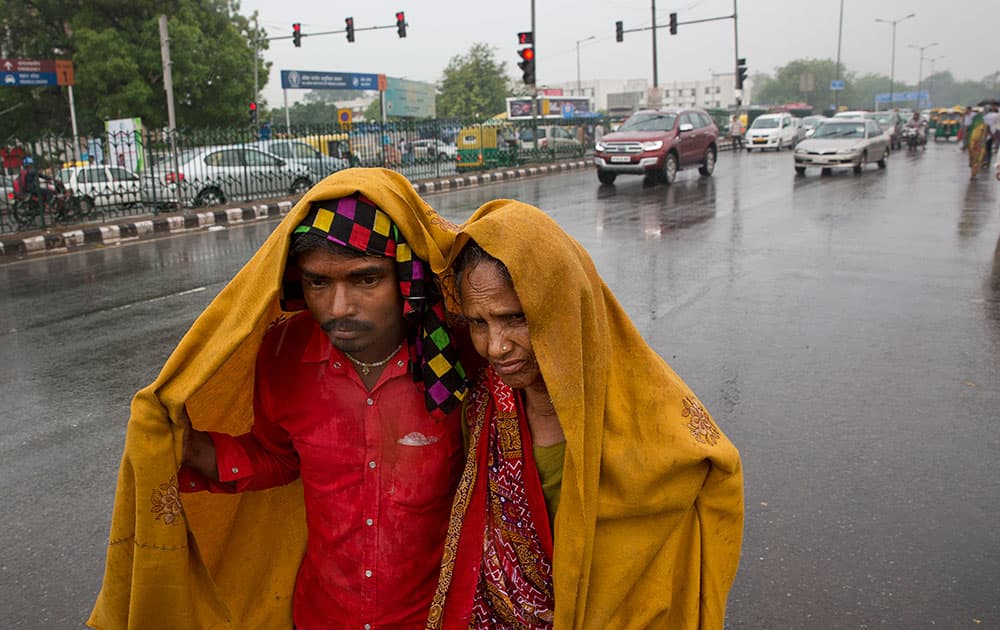 A son covers her mother with a shawl in the rain, as they look for transportation in New Delhi.