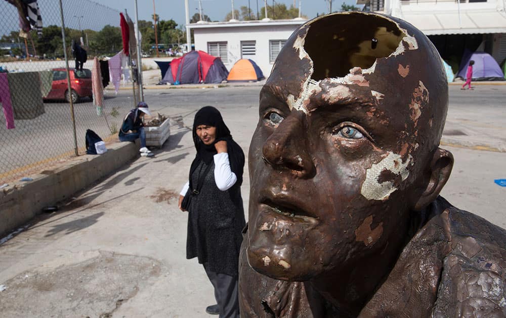 An Afghan woman stands behind the broken head of a statue at the west terminal of an abandoned old airport which is used as a shelter for over 3,500 migrants, in southern Athens.