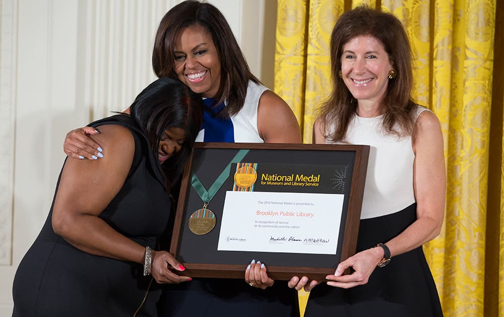 First lady Michelle Obama hugs Kim Best, left, accompanied by Linda Johnson, as the Brooklyn Public Library receives a 2016 National Medal for Museum and Library Service award during a ceremony in the East Room of the White House.