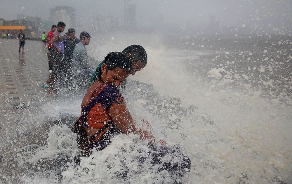 A couple gets drenched in a wave hitting the shore during high tide