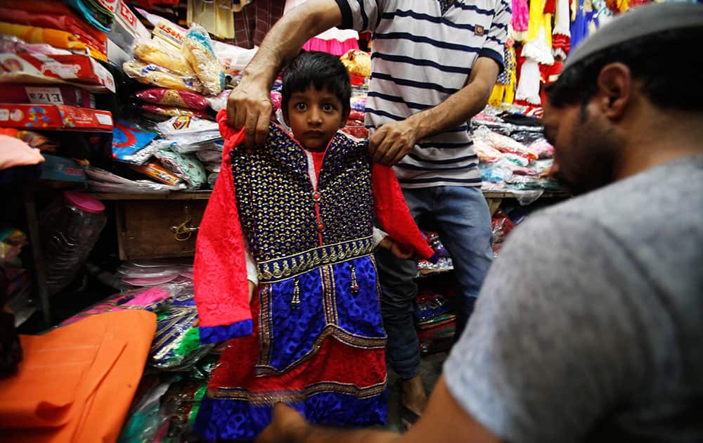 A man holds up a dress for size on a Kashmiri child ahead of Eid al-Fitr in Srinagar