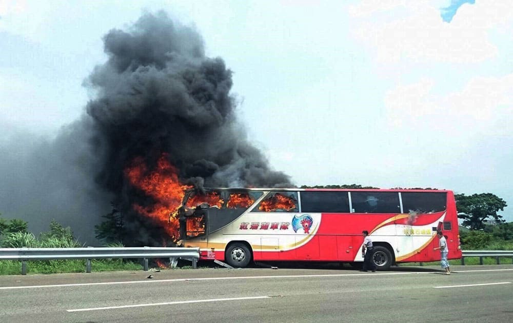 A policeman and another man try to break the windows of a burning tour bus on the side of a highway in Taoyuan, Taiwan.