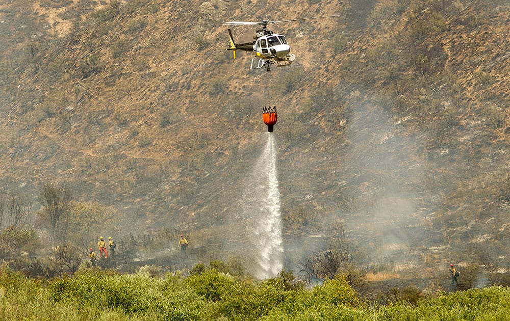 A helicopter drops water on a wildfire