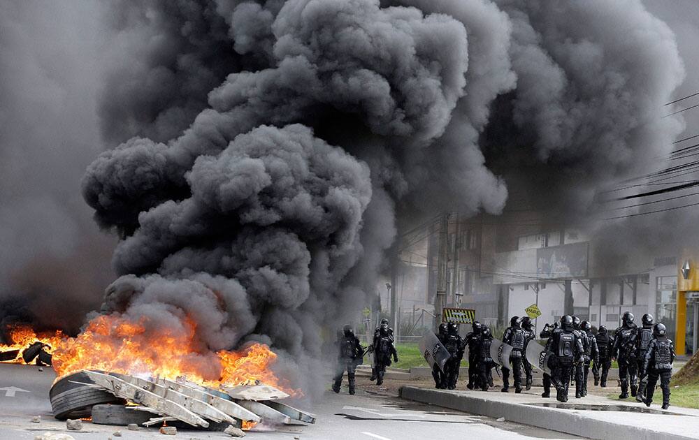 Riot police walk past a flaming barricade set by striking truckers in Bogota